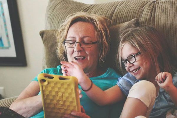 A woman and a little girl are sitting on a couch looking at a tablet.