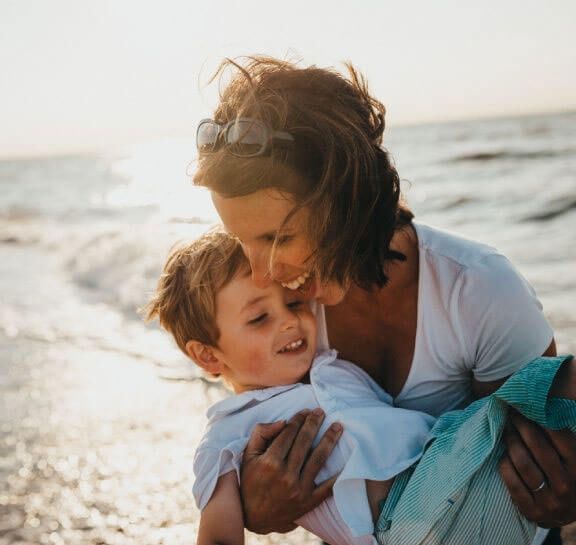 A woman is holding a little boy on the beach.