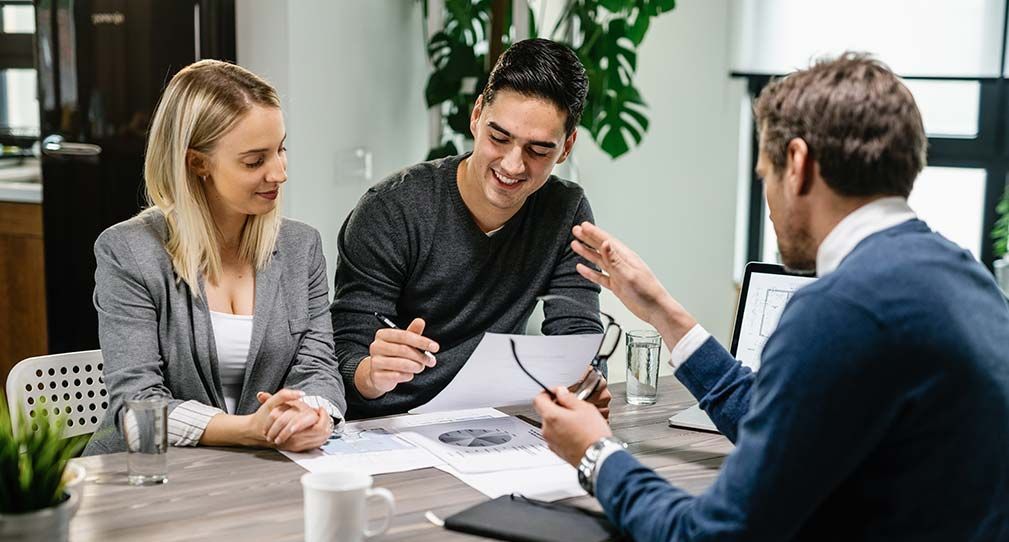 A man and a woman are sitting at a table talking to a man.