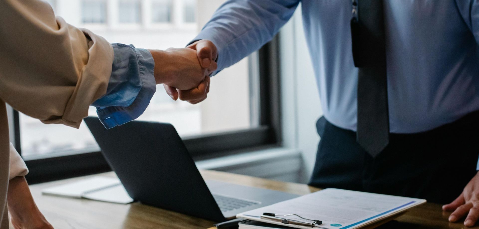 A man and a woman are shaking hands in front of a laptop.