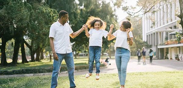 A family is holding hands and jumping in the air in a park.