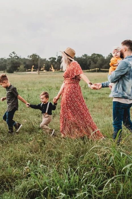 A family is walking through a grassy field holding hands.