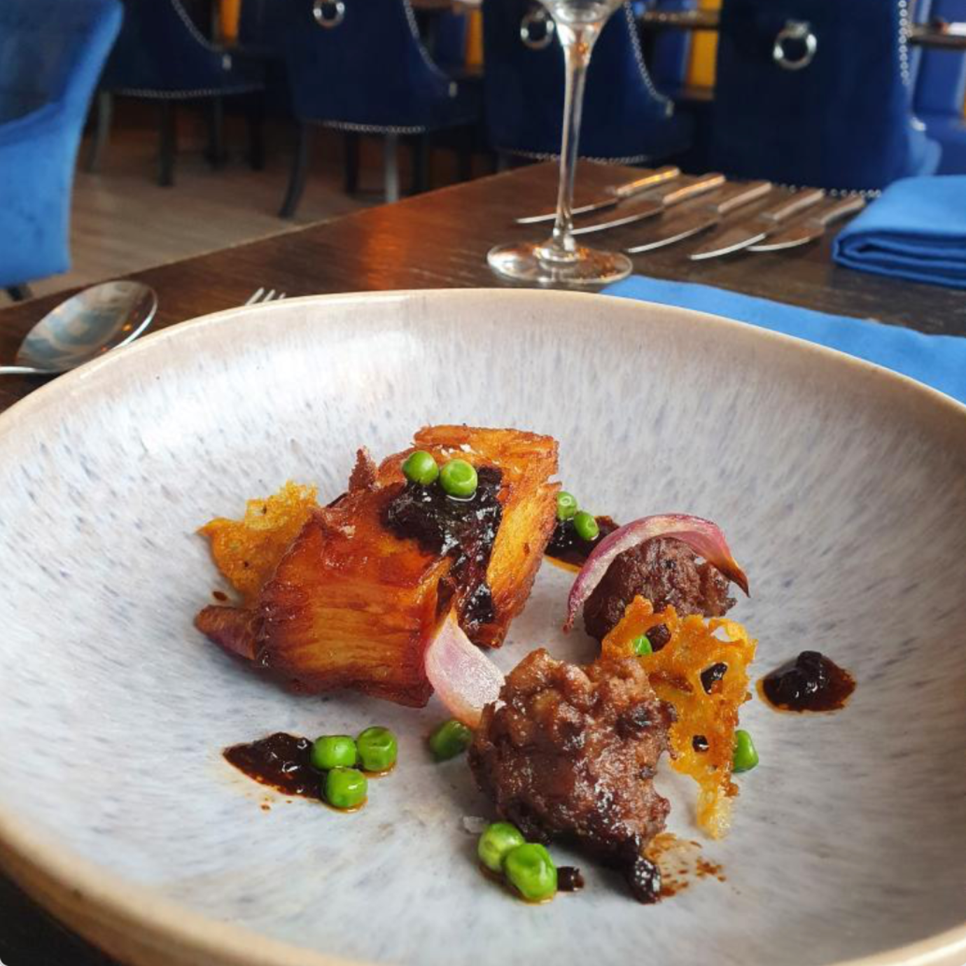 Gourmet plate of food: potato, meat, peas, onion, and sauce on a speckled white plate in a restaurant.