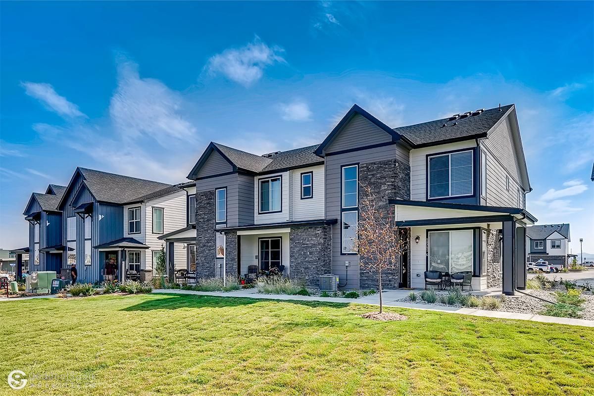 Row of modern two-story townhouses with stone facades and a green lawn under a blue sky