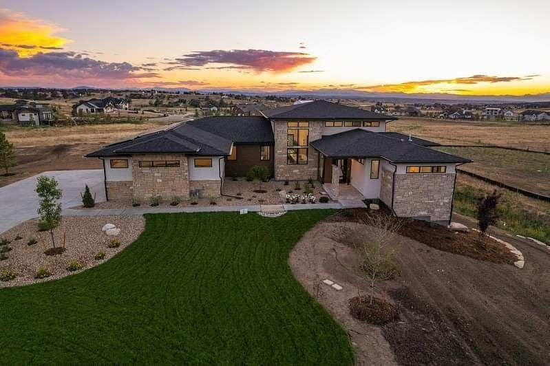 Modern stone house at sunset with landscaped lawn and desert surroundings