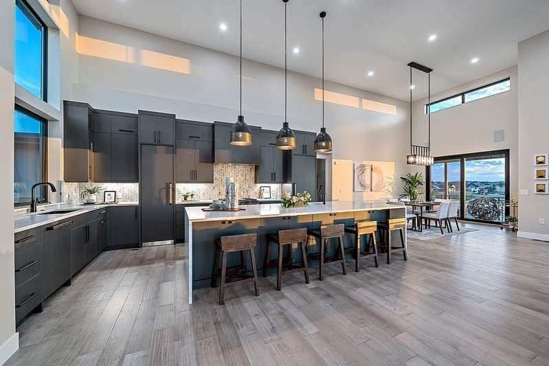Modern open-plan kitchen with dark cabinets, long island, pendant lights, and large windows.