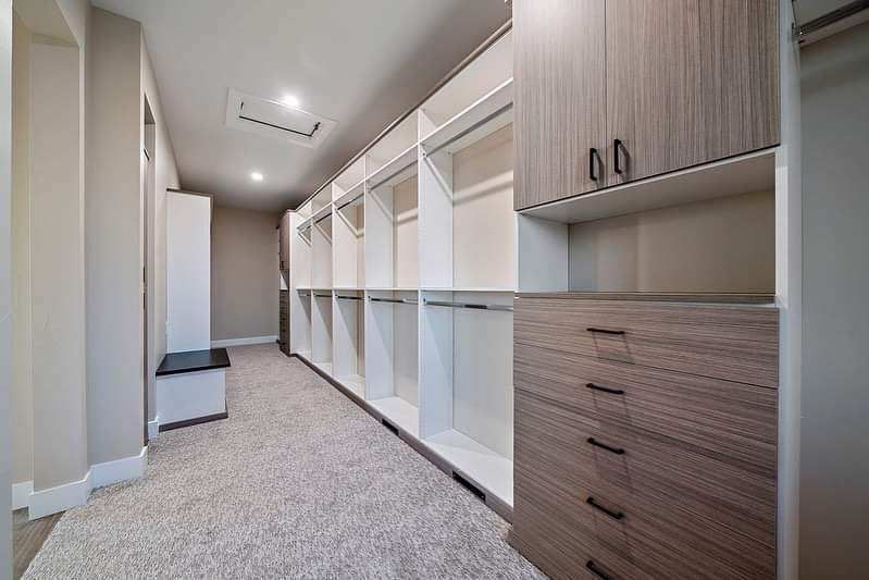 Long walk-in closet with white shelving, wood cabinets, and carpeted floor