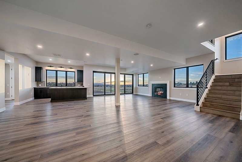 Spacious modern living room with wood floors, large windows, kitchen island, and staircase to the right