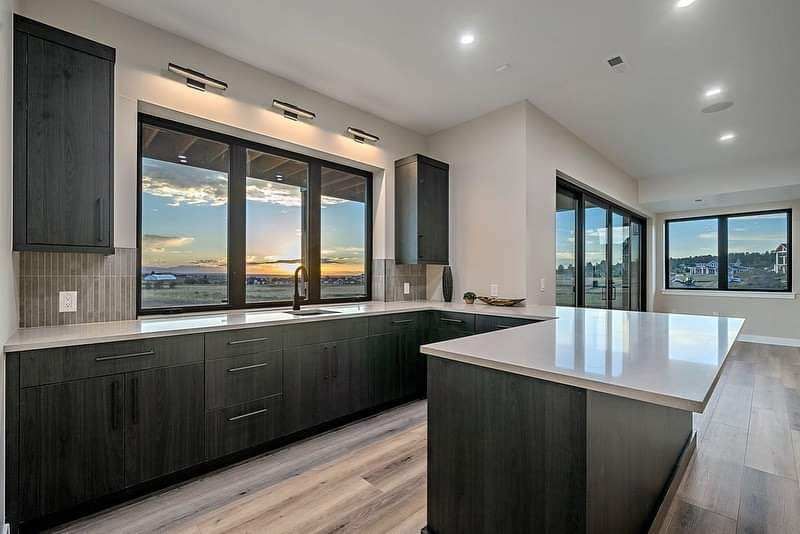 Modern kitchen with dark cabinets, white island, and large windows overlooking a sunset view