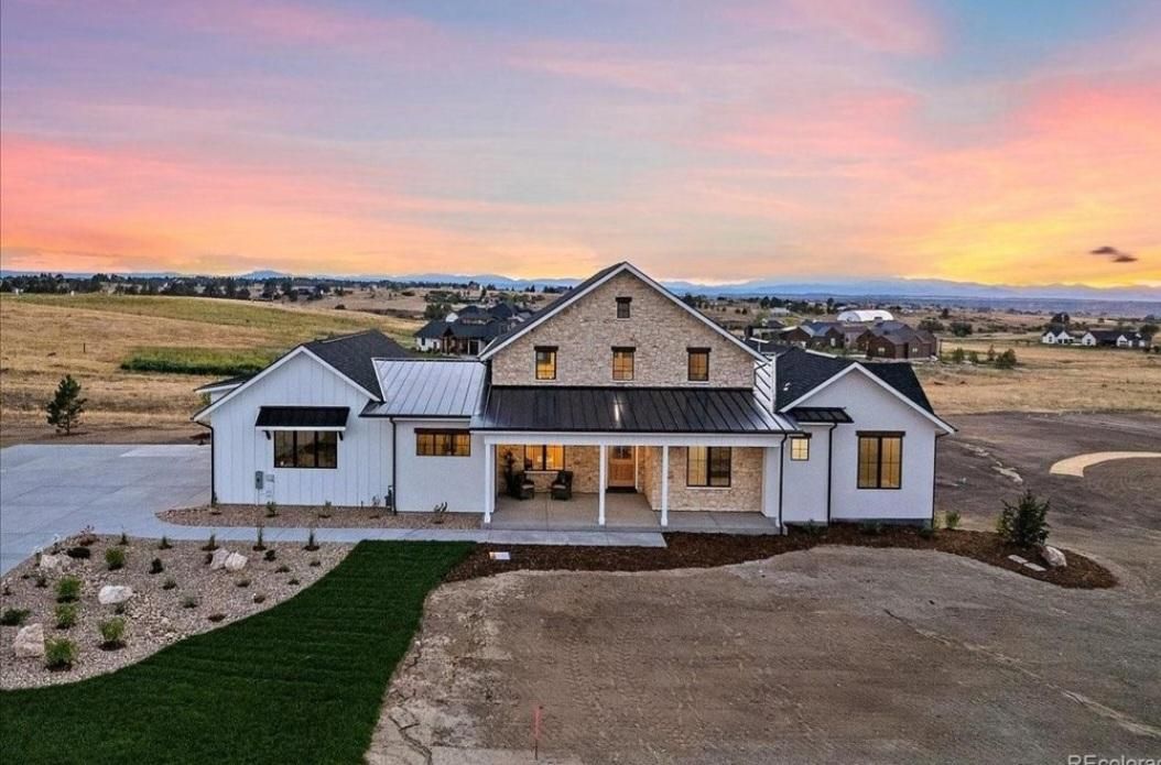 Modern farmhouse exterior at sunset with white siding, stone accents, and a large front yard.