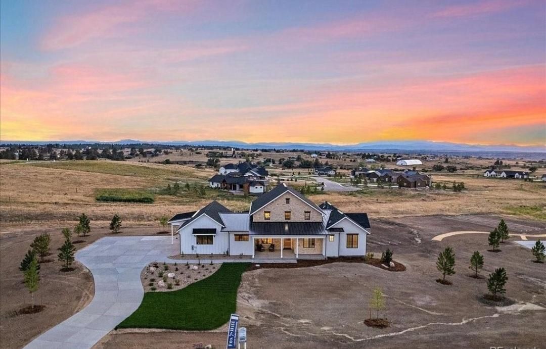 Luxury house at sunset with a winding driveway, dry landscape, and colorful sky.