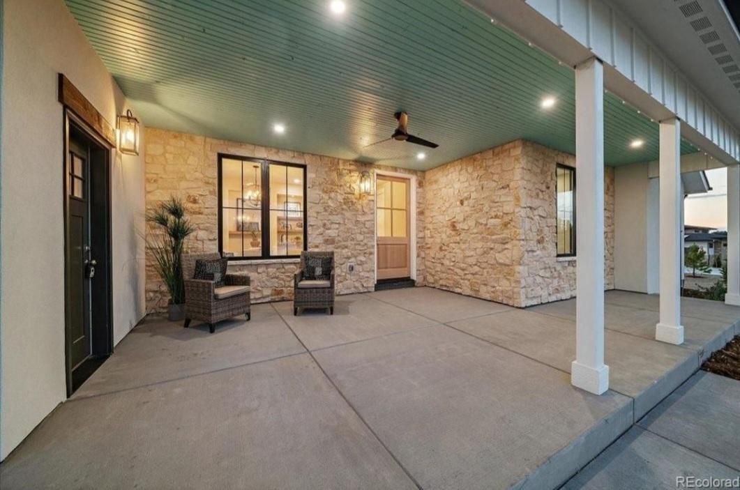 Covered outdoor patio with two chairs and a table beside a brick wall and white columns