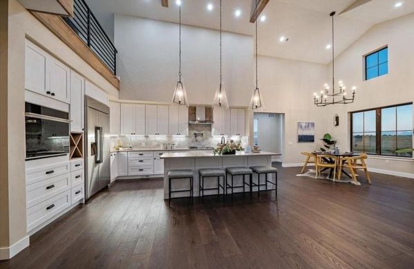 Modern open-plan kitchen and dining room with white cabinets, dark wood floors, island, and pendant lights