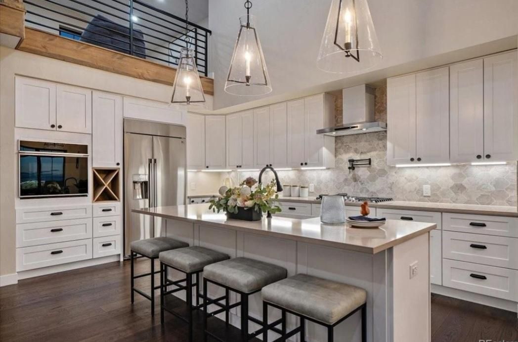 Modern white kitchen with island, bar stools, pendant lights, and stainless steel appliances