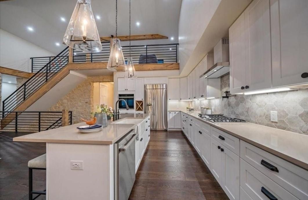 Modern open-plan kitchen with white cabinetry, island, staircase, and chandelier in a bright home