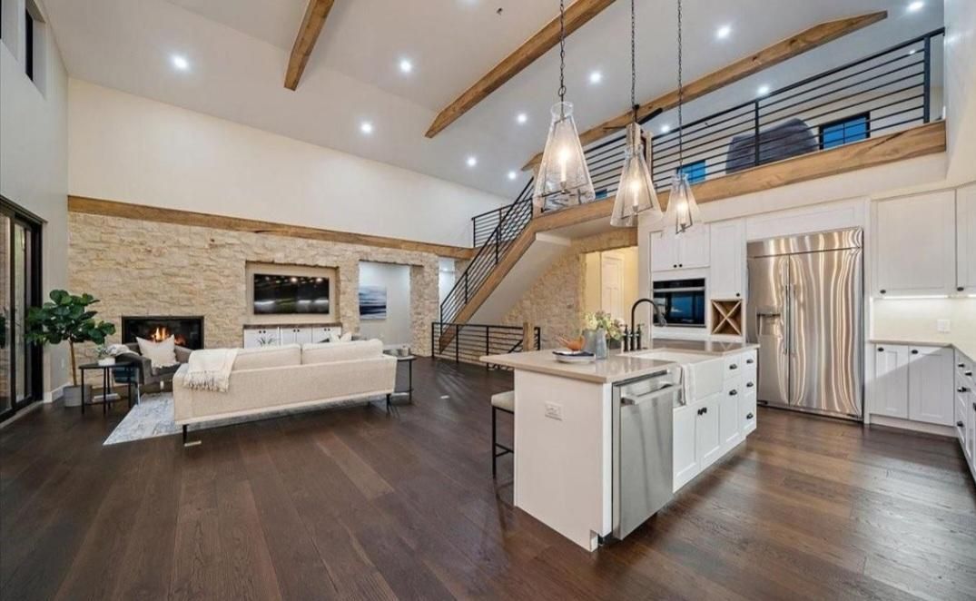 Spacious modern living room with kitchen island, staircase, chandelier, and dark wood floors