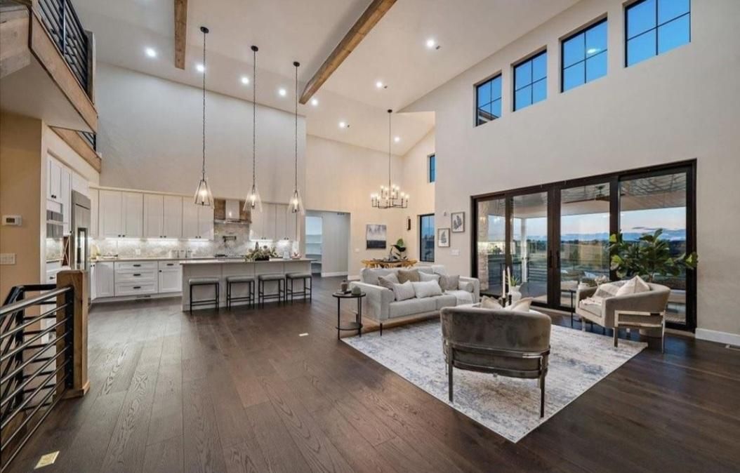 Spacious modern living room with vaulted ceilings, kitchen island, and large glass doors opening to a patio