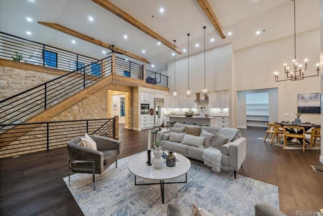 Spacious modern living room with high ceilings, gray sofa, staircase, and warm wood accents