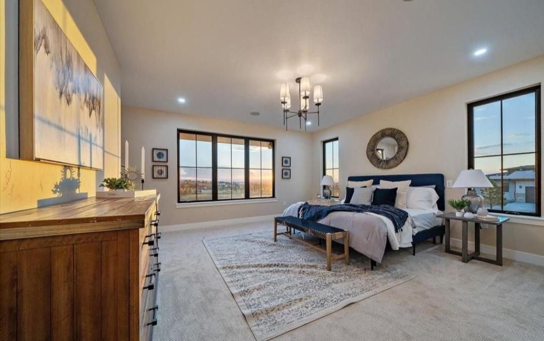 Modern bedroom with king bed, bench, chandelier, large window, and ocean-view balcony.