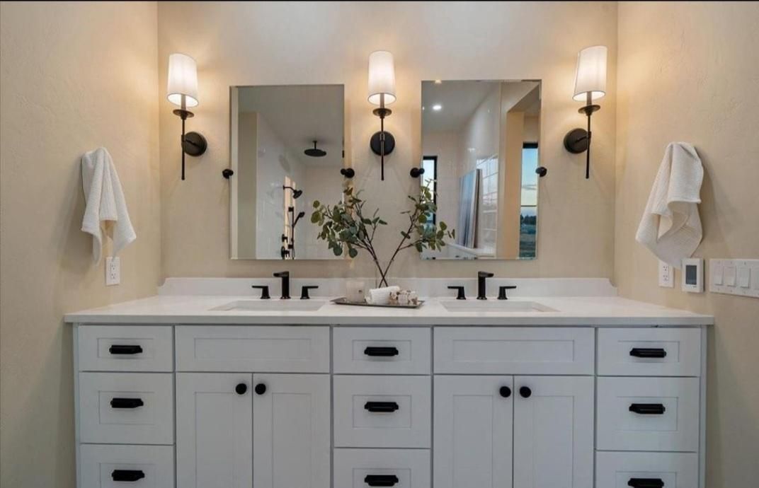 Double vanity bathroom with white cabinets, beige walls, mirrors, sconces, and towels.