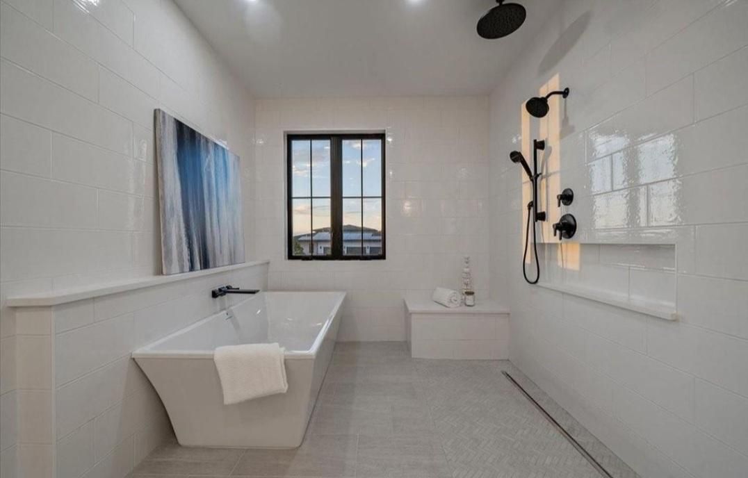 Modern white bathroom with freestanding tub, walk-in shower, and small window above a tiled floor
