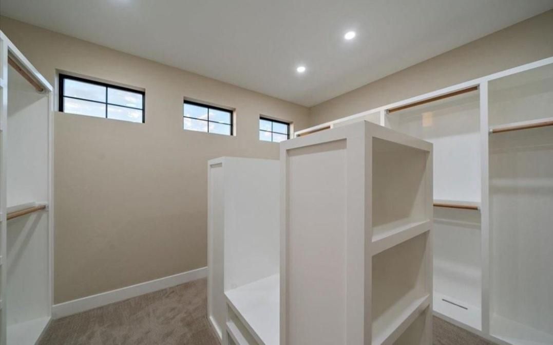 Empty walk-in closet with white shelving, beige walls, and small high windows