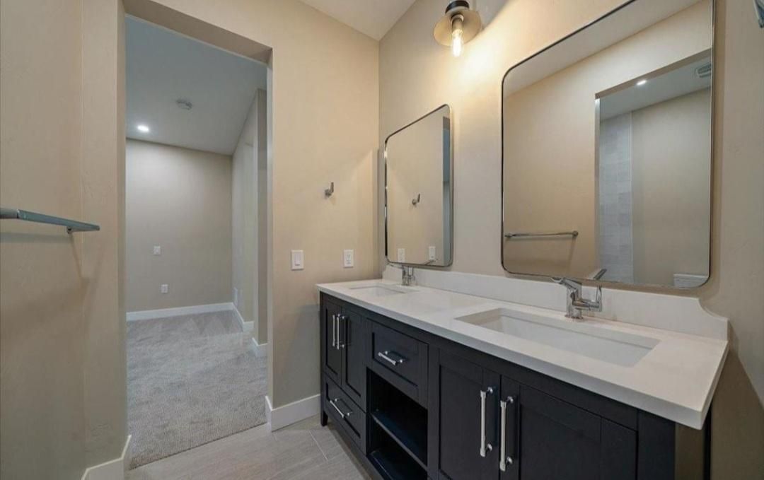Modern bathroom vanity with double sinks, large mirrors, and a walk-in shower entrance in the background