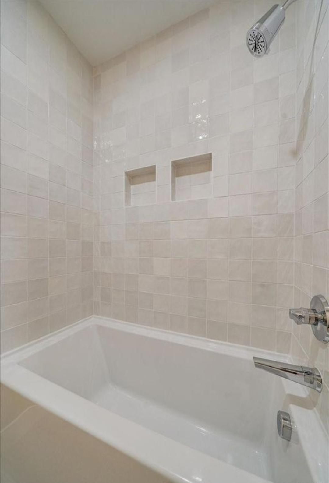 Small beige-tiled bathroom with a white bathtub and showerhead.