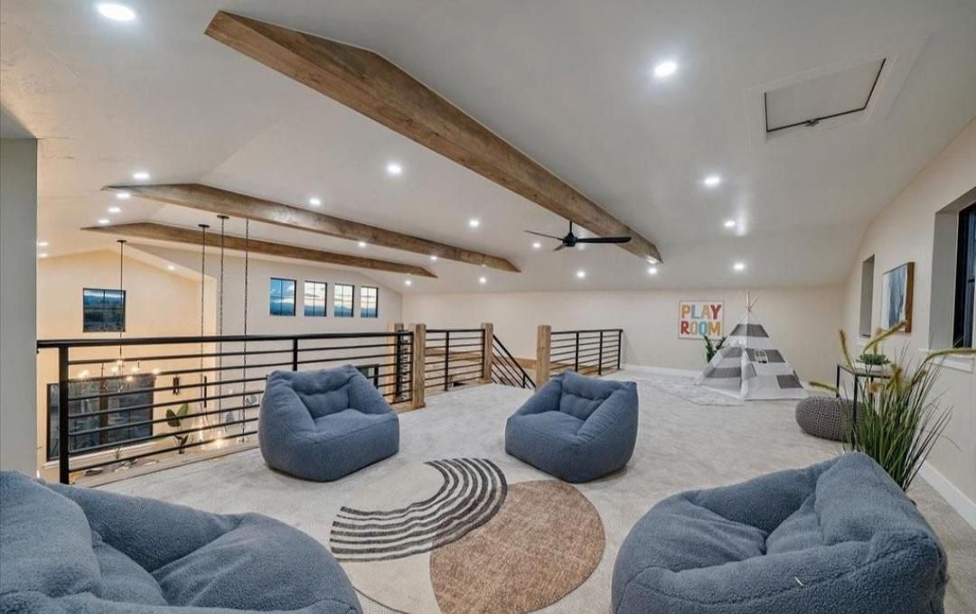 Bright modern lounge with gray beanbags, wood beam ceiling, railings, and abstract wall art