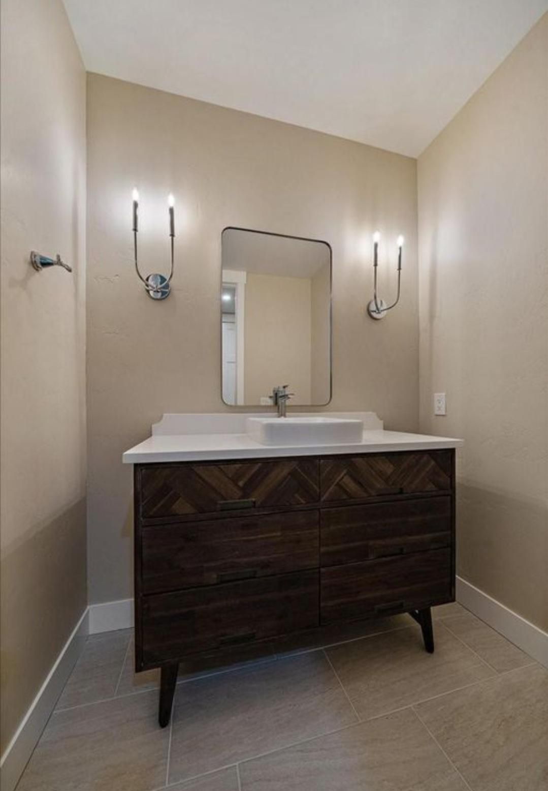 Small beige bathroom with a white sink vanity, mirror, and wall sconces