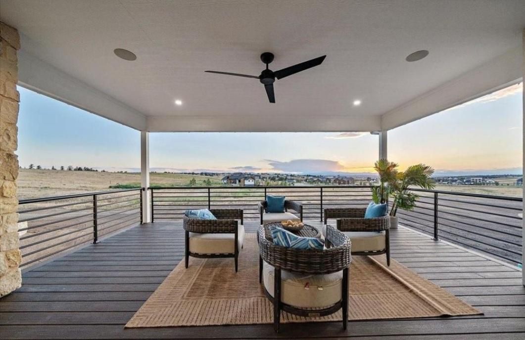 Covered patio overlooking water at sunset, with wicker seating, ceiling fan, and lounge chairs on a wooden deck