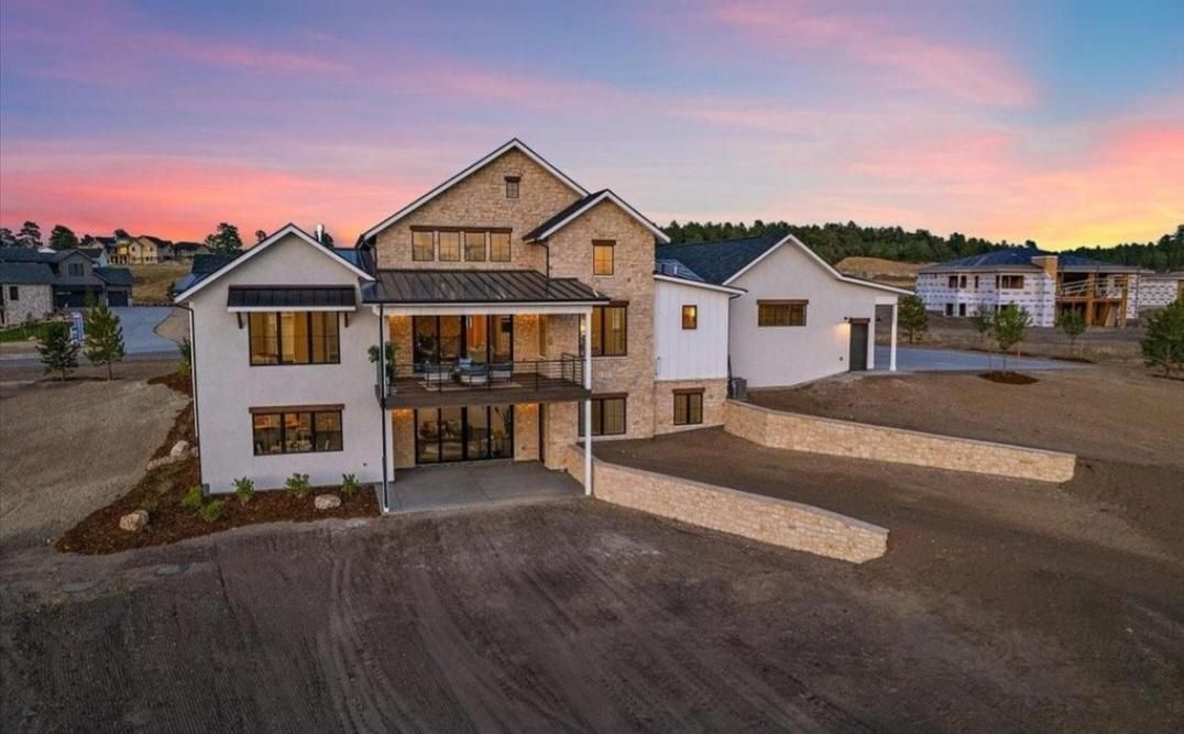 Modern two-story house under construction at dusk with unfinished landscaping and a pink sky