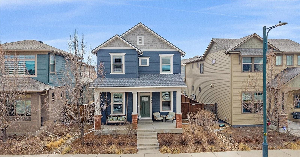 Blue two-story house centered between beige homes on a quiet residential street.