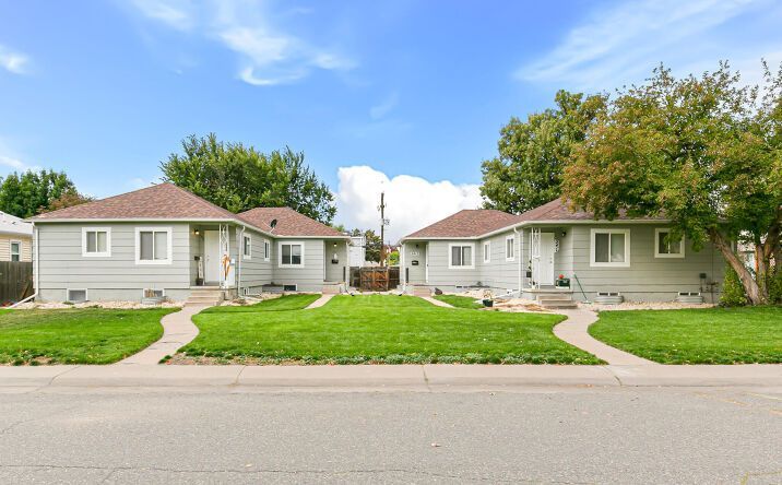 Two single-story gray homes with red roofs and green lawns along a quiet residential street.