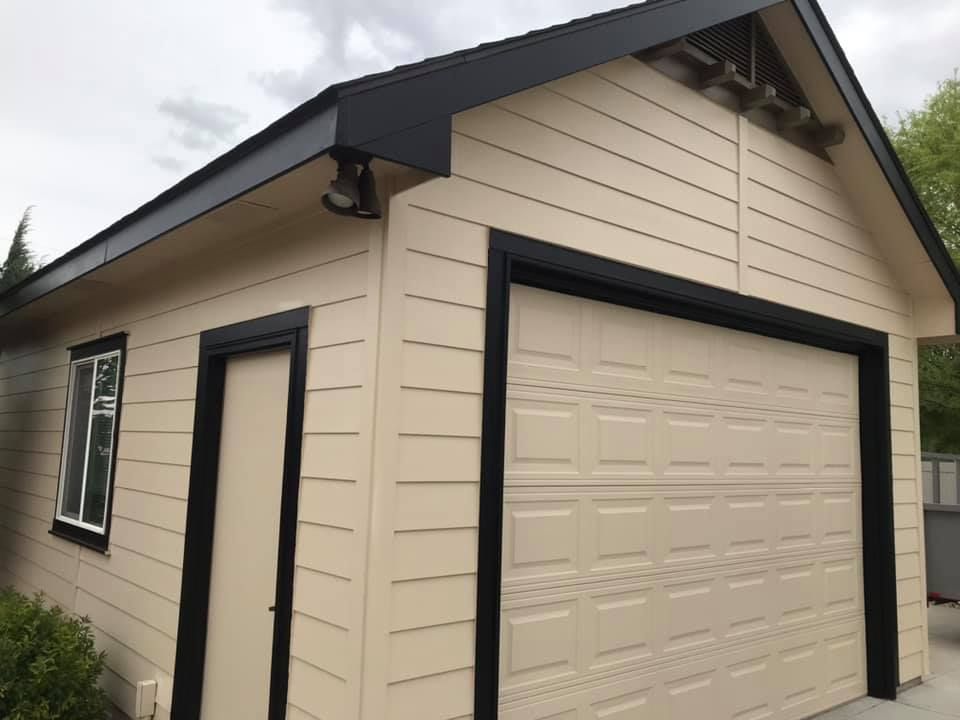 Beige detached garage with black trim and a single white garage door under a gabled roof