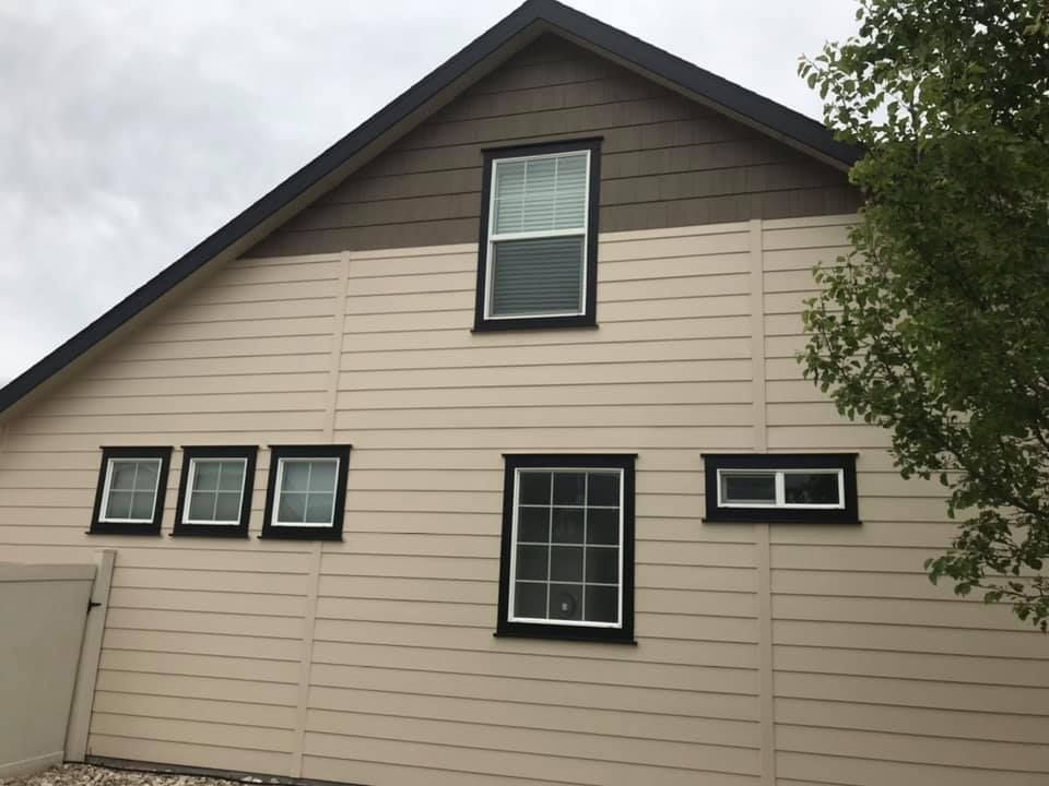 Tan house exterior with black-trimmed windows and a steep gable roof under cloudy sky