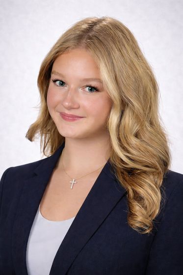 Portrait of a smiling person in a navy blazer and white top against a light gray background