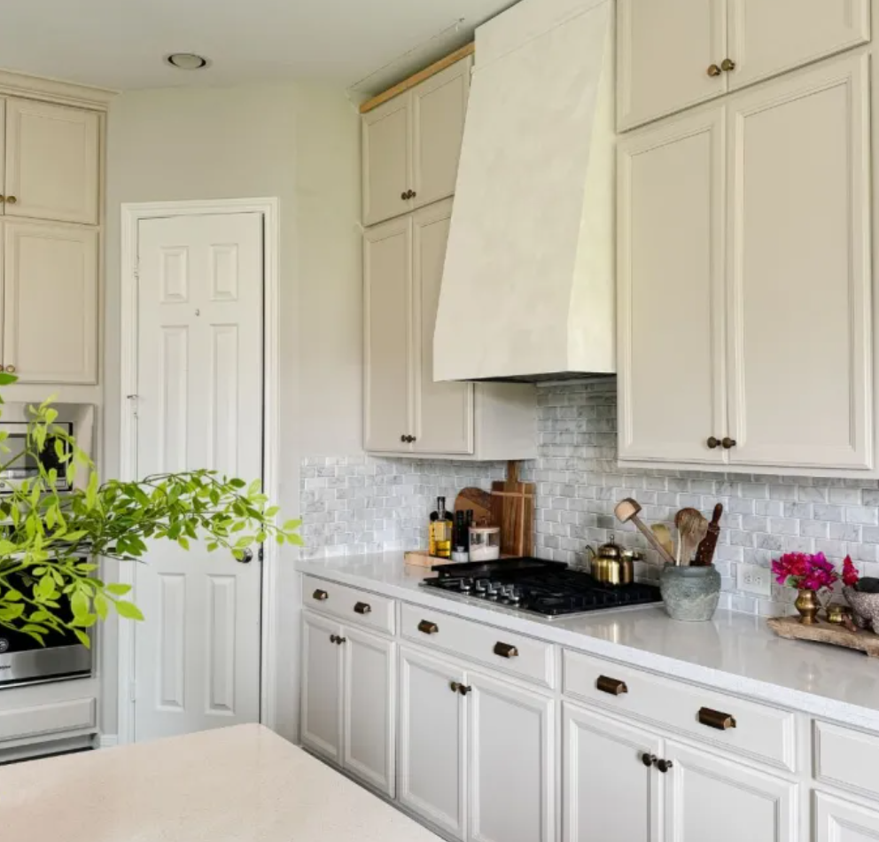 Bright white kitchen with cabinets, marble countertops, and a gas stove under a vent hood.