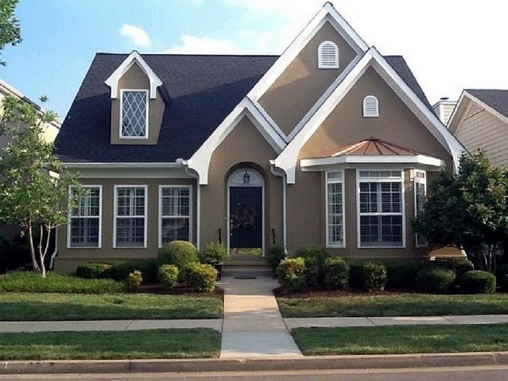 Suburban house with beige siding, white trim, dark roof, and a front walkway bordered by shrubs.