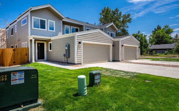 Modern two-story beige townhouse with a garage and green lawn under a clear blue sky