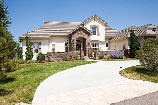 Large beige suburban house with stone accents and a curved white driveway under a blue sky
