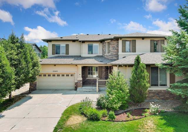 Suburban two-story beige house with a garage, driveway, and landscaped front yard under a blue sky