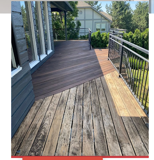 Weathered wooden deck with dark composite section, black railing, and a house in the background