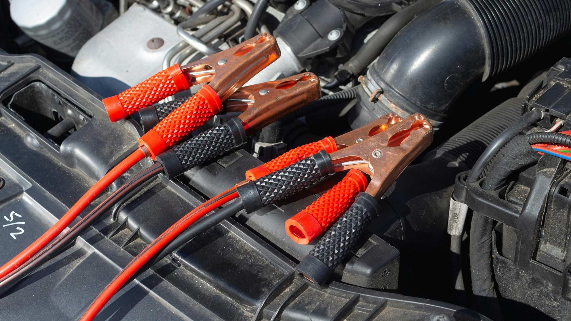 Red and black alligator clips attached to car battery terminals under the hood.