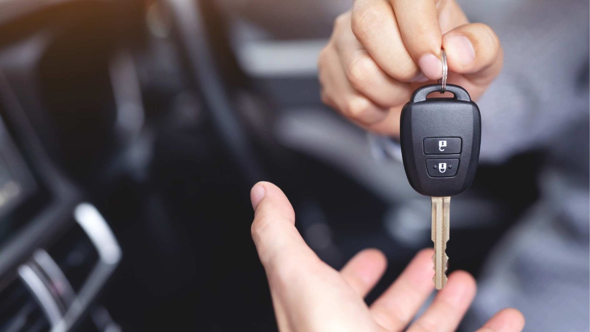 A person holding a car key near a vehicle ignition, with a dashboard visible in the background.