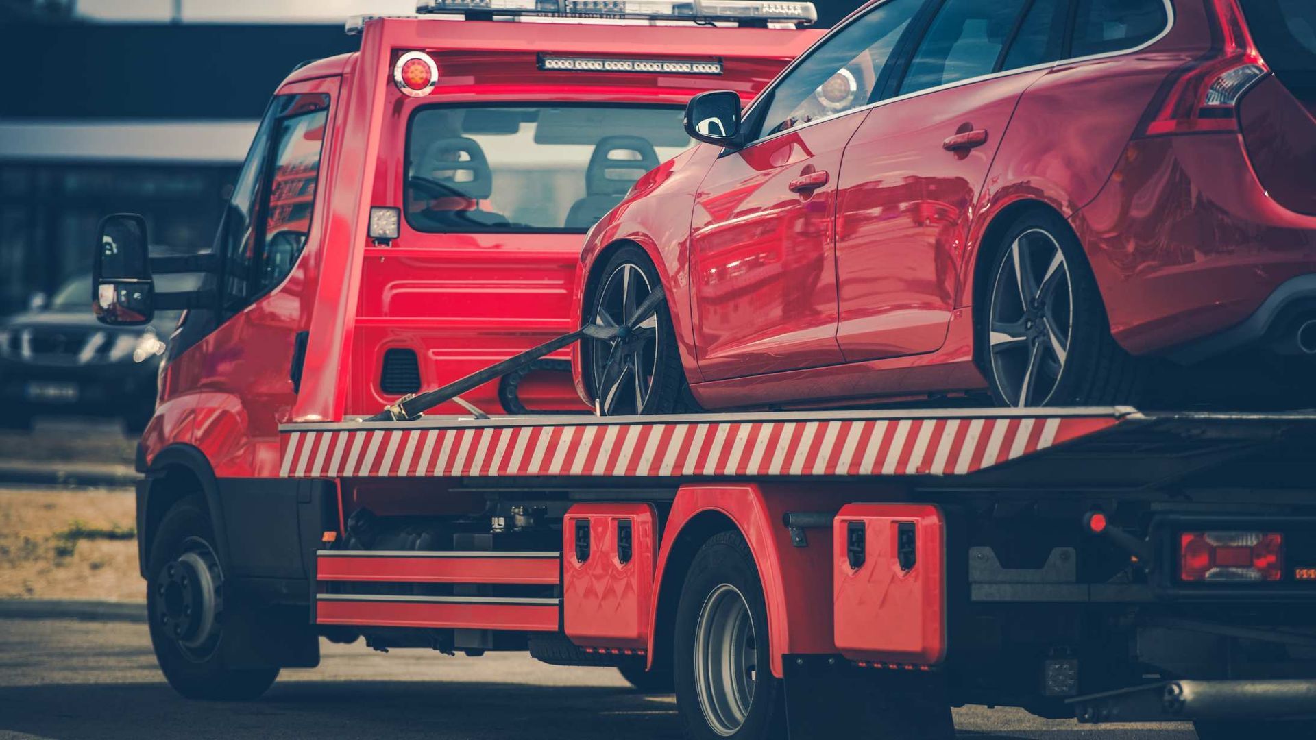 Red car loaded on a tow truck flatbed in an outdoor roadside setting.