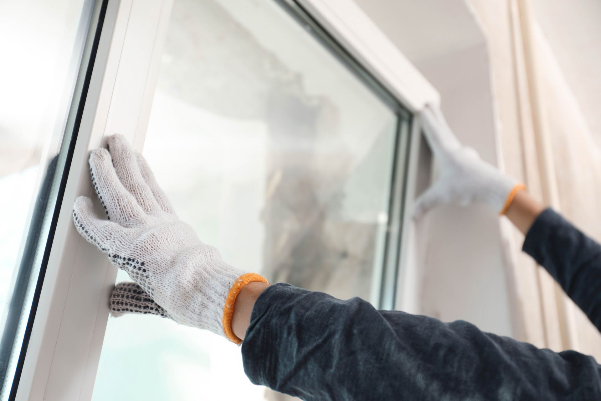 A gloved installer is fitting a replacement window panel into the frame.
