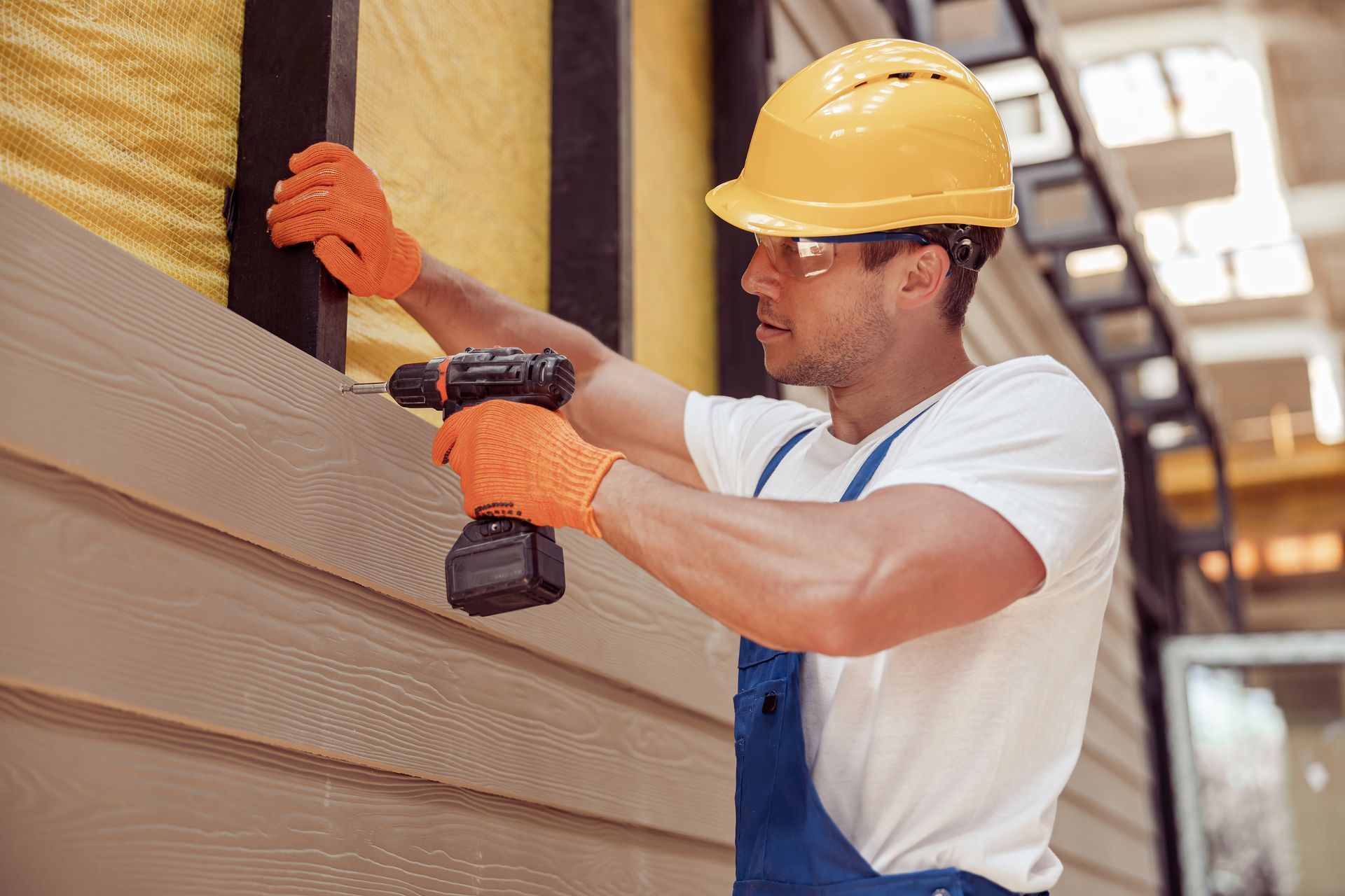 A professional siding contractor installing new vinyl planks on the exterior of a modern home. A professional siding contractor installing new vinyl planks on the exterior of a modern home.