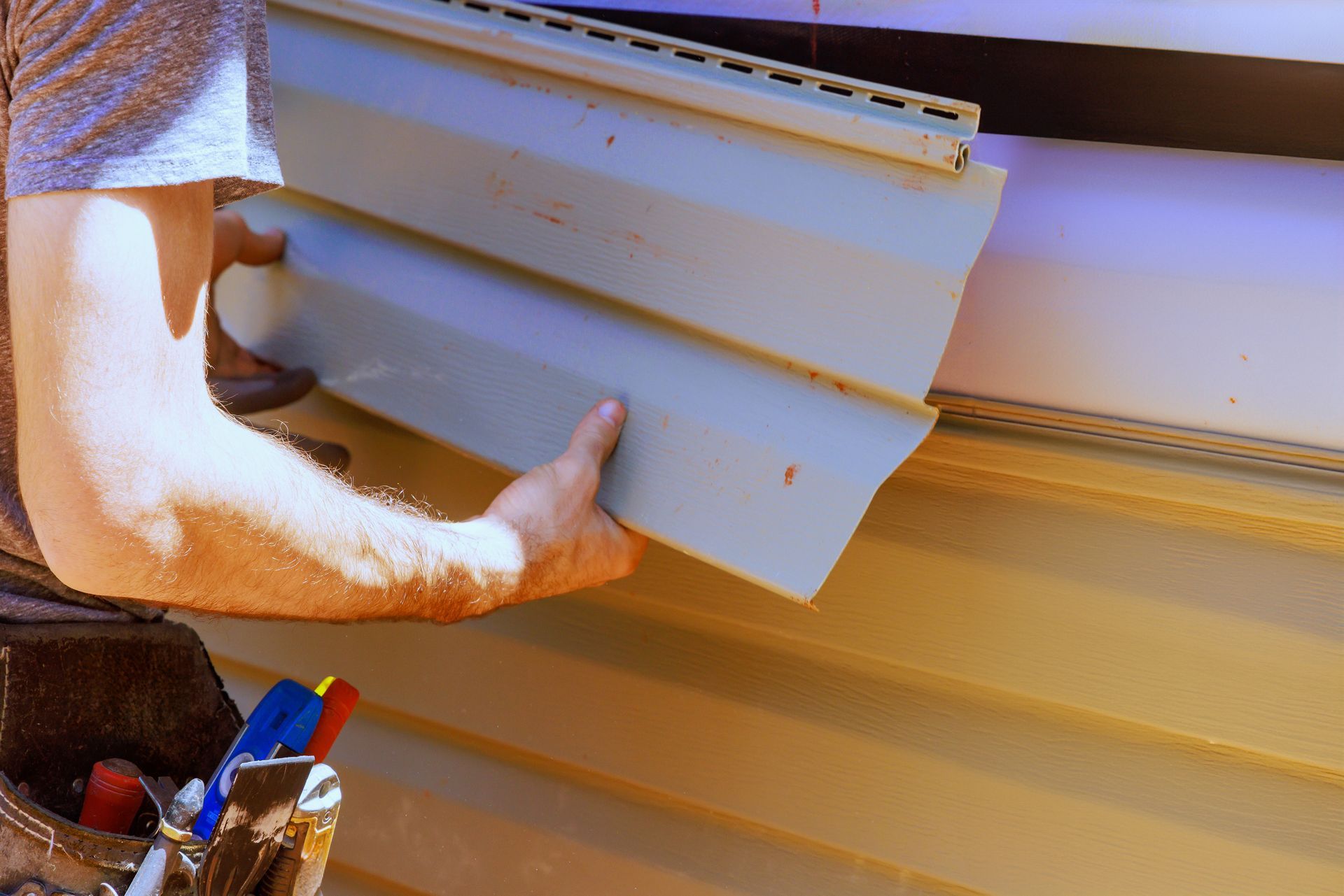 As part of construction, a worker installs vinyl siding panels on a house facade. As part of construction, a worker installs vinyl siding panels on a house facade.