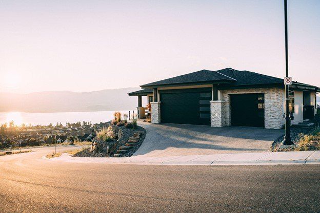 A large house with two garages is sitting on top of a hill next to a lake | Siefken Roofing and Remodeling Services in Omaha, NE